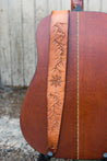 Details of hand tooled topographic mountains and compass rose on leather guitar strap