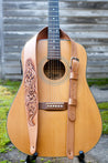 Leather guitar strap with intricate hand carved scrollwork shown on guitar 
