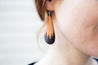 Model wearing handcrafted leather teardrop earrings with a custom stamped forest design.