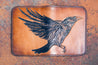 Flat-lay of handcrafted leather wallet with raven design hand-tooled on the front