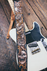 Hand carved leather Skulls and Roses guitar strap resting on electric guitar. Tooled design runs full length of strap.