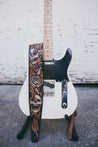 Hand carved leather Skulls and Roses guitar strap draped over electric guitar. 