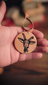 Hand holding a handcrafted leather ornament with the Spokane Garbage Goat design against a blurred background