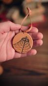 Hand holding a handcrafted leather ornament with the Spokane Pavilion design against a blurred background