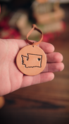 Hand holding a leather ornament with a Washington state outline and heart in the location of the city of Spokane
