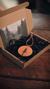 Leather ornament with tree design in an open box on a wooden surface