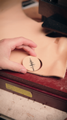 Person holding a circle of leather with an embossed pine tree design on a leather press