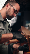Man wearing black gloves punching a small hole in a leather ornament with a blurred background