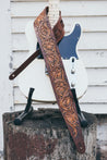 Hand carved leather Sheridan rose guitar strap draped over electric guitar. Tooling runs full length of strap.