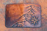 Flat-lay of handcrafted leather wallet with Cascadia mountain design hand-tooled on the front