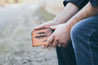 Man holding handcrafted leather wallet with tooled lodgepole pine forest design on front